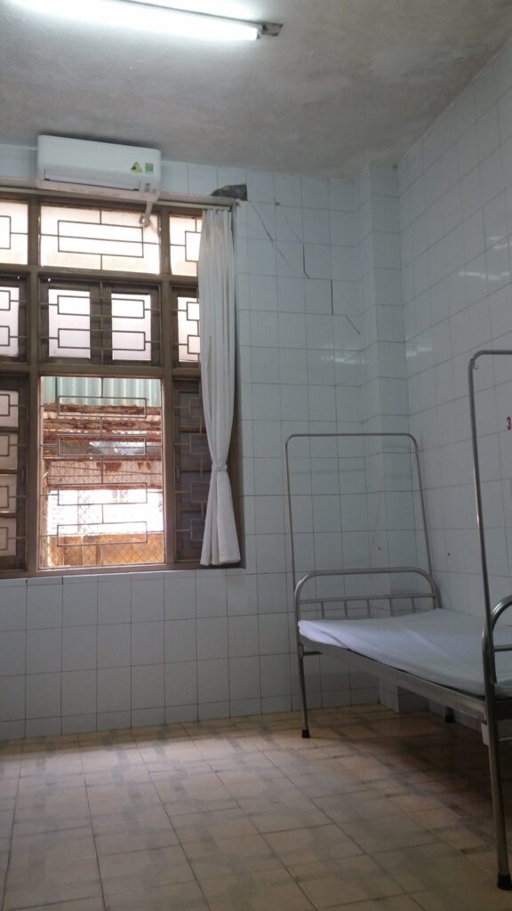 Basic hospital room in Vietnam with single bed, tiled walls, and minimal facilities