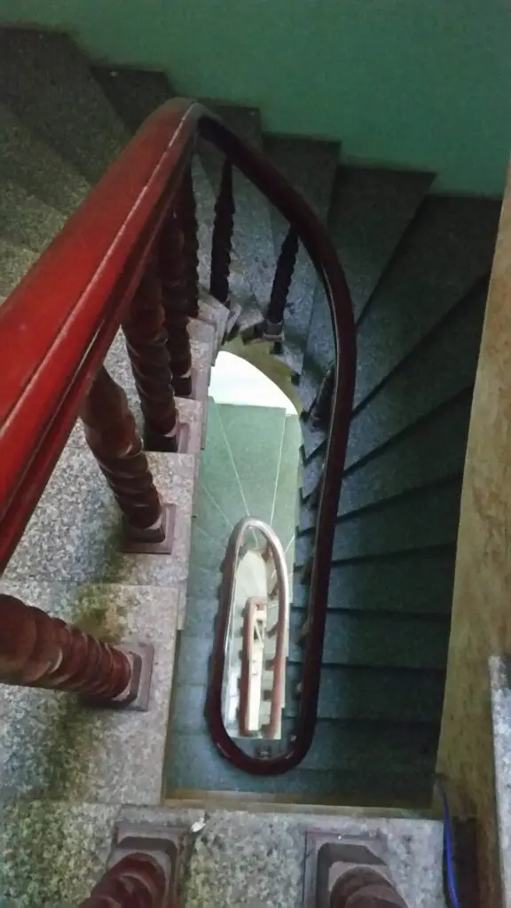 Narrow spiral staircase in Vietnam with steep steps and wooden handrail