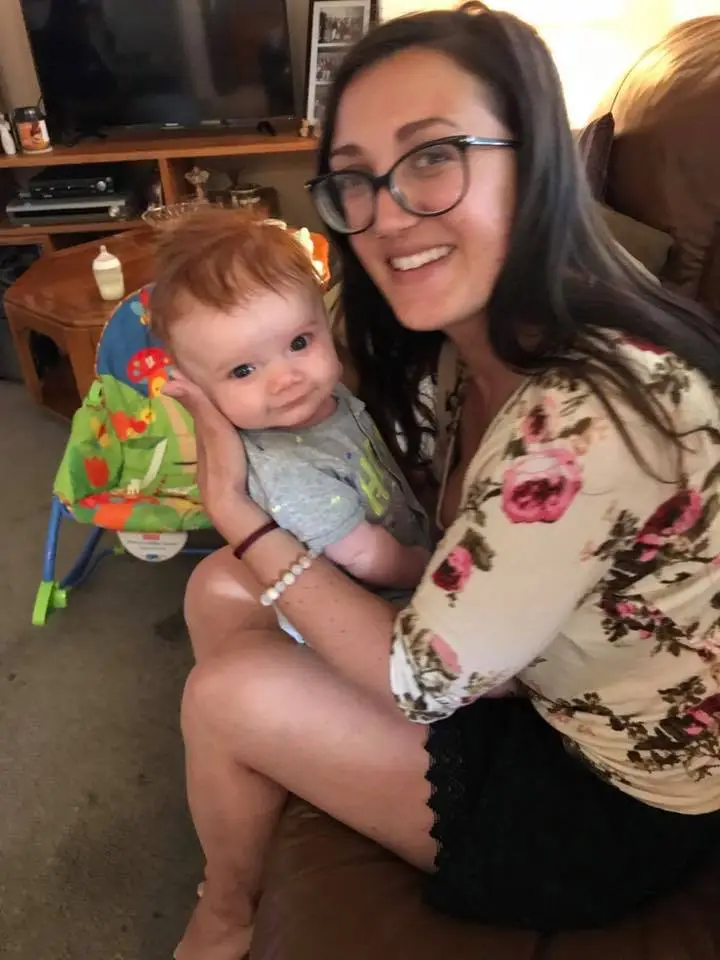 Woman holding a baby while smiling indoors