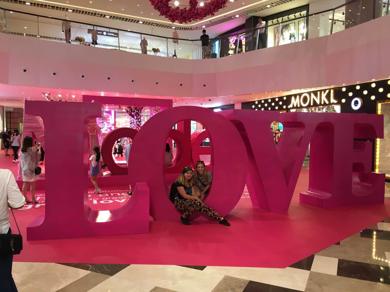 Two women posing beside a large pink LOVE sign in a shopping mall in Shanghai