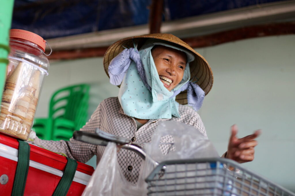 Smiling street vendor in Vietnam wearing traditional hat beside bicycle