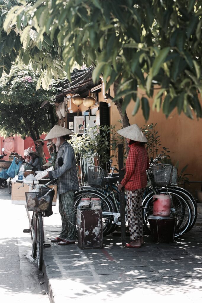 Two women in conical hats standing with bicycles on a street in Vietnam