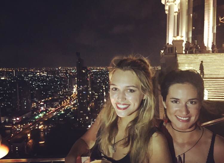 Two women at a Bangkok rooftop bar overlooking the city skyline at night