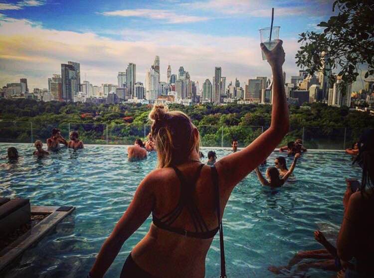 Infinity pool rooftop party in Bangkok with city skyline view and people relaxing