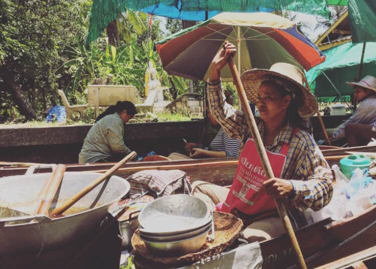 Vendor at Damnoen Saduak floating market selling goods from a boat in Thailand