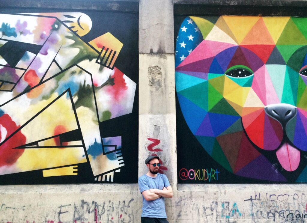 Man standing between two large street art murals in Madrid.