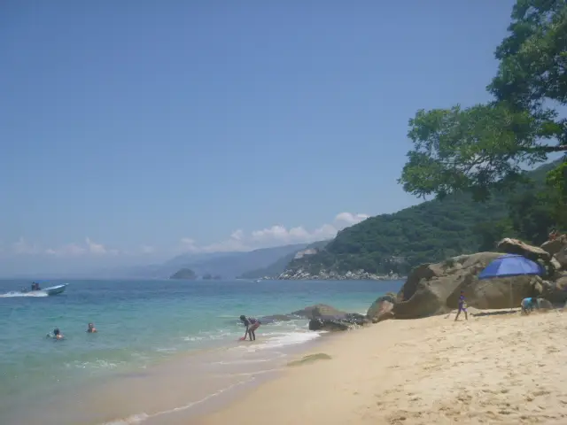 Sandy beach with people swimming and relaxing near rocky coastline and clear blue sea in Puerto Vallarta