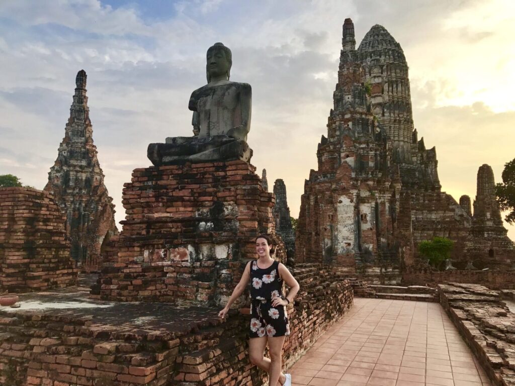 Woman standing beside ancient temple ruins and a large seated Buddha statue in Ayutthaya, Thailand