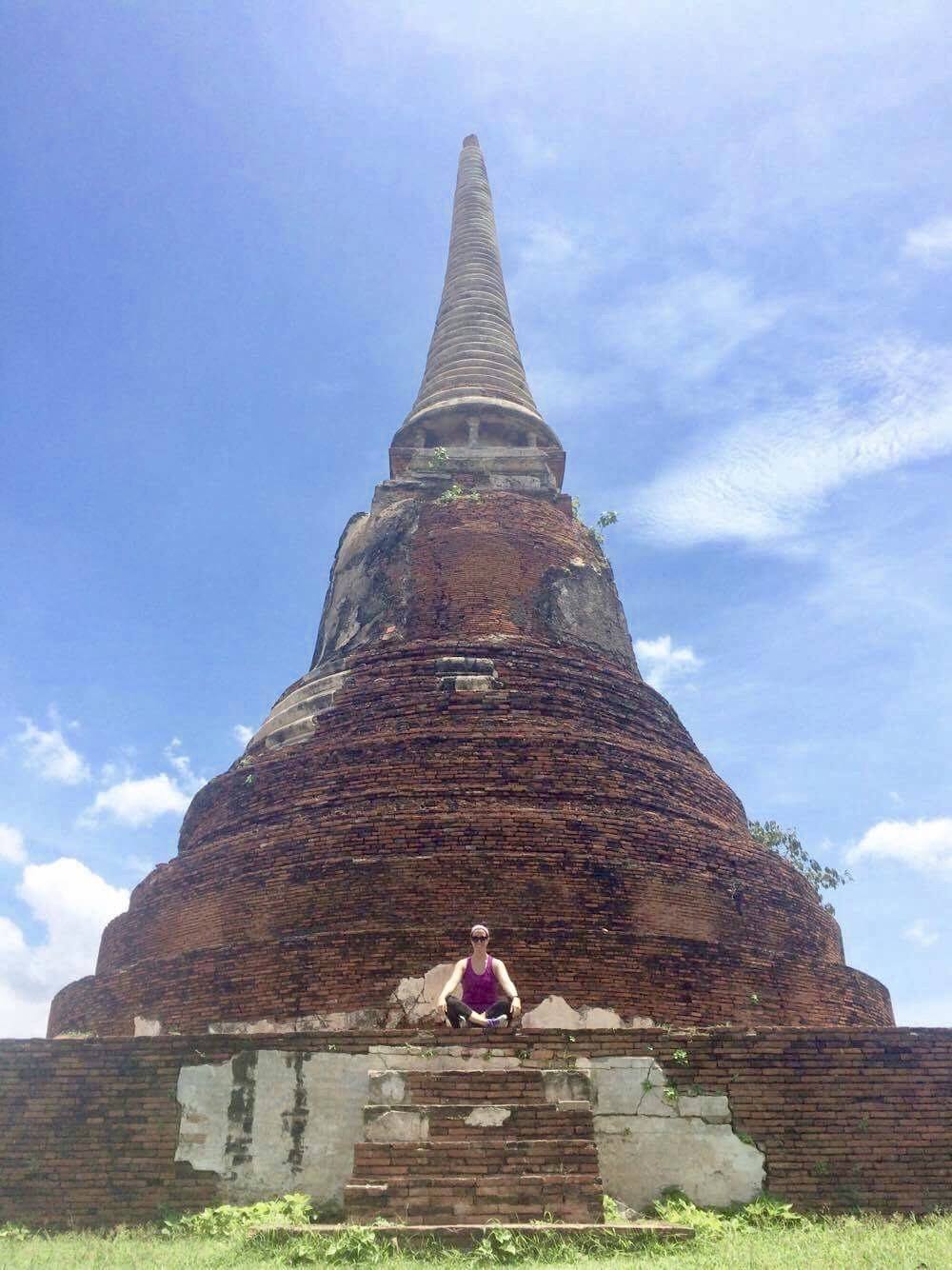Woman sitting in front of a large historic chedi at an ancient temple in Ayutthaya, Thailand