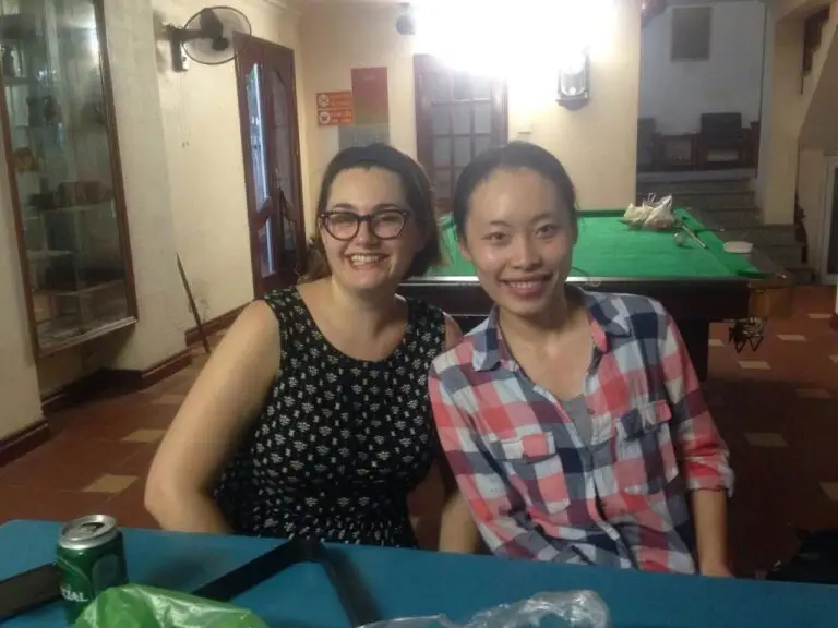 Teacher and local friend sitting together indoors in Vietnam smiling at the camera